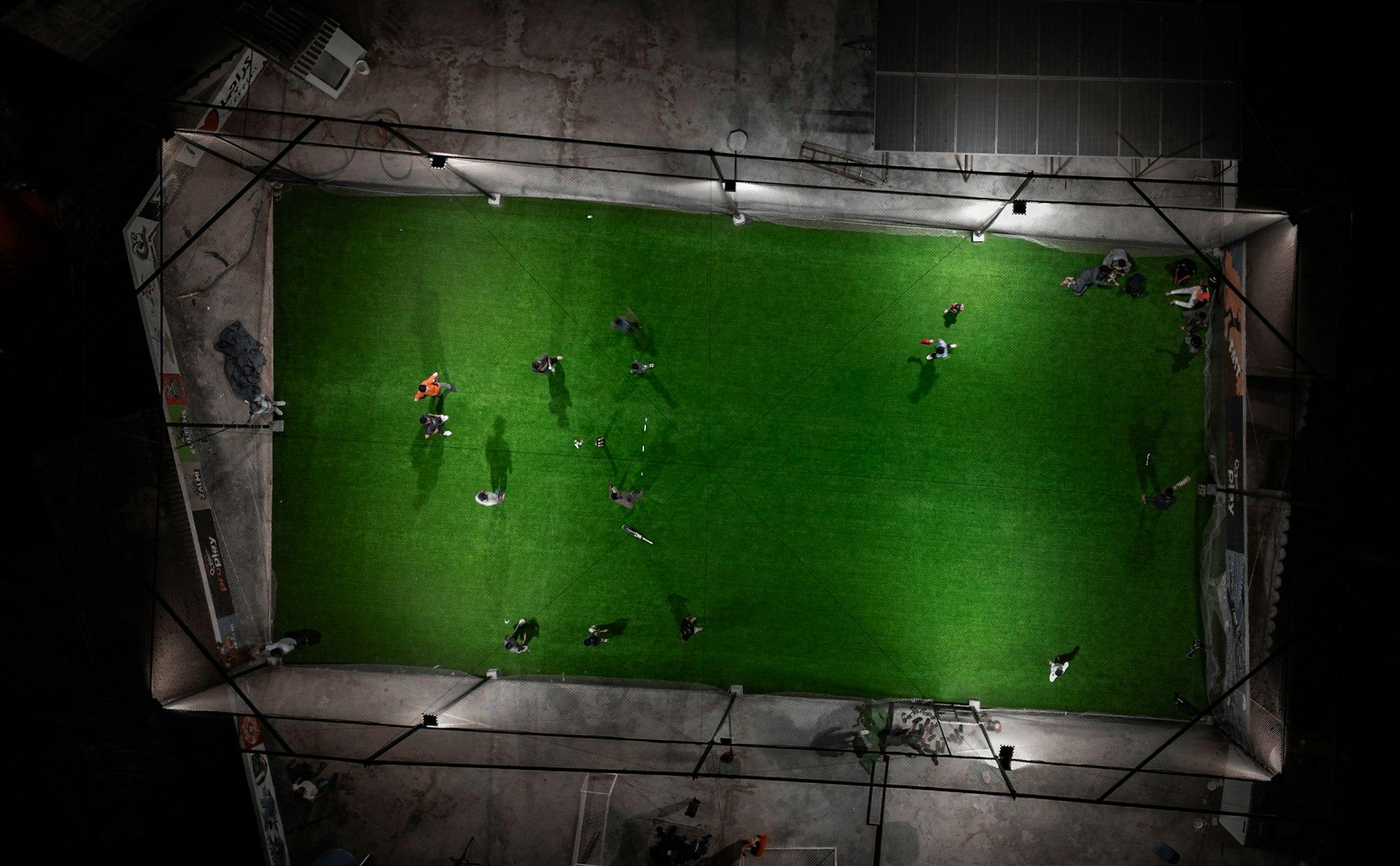 Omsloten voetbalveld van bovenaf, met spelers onder de lampen